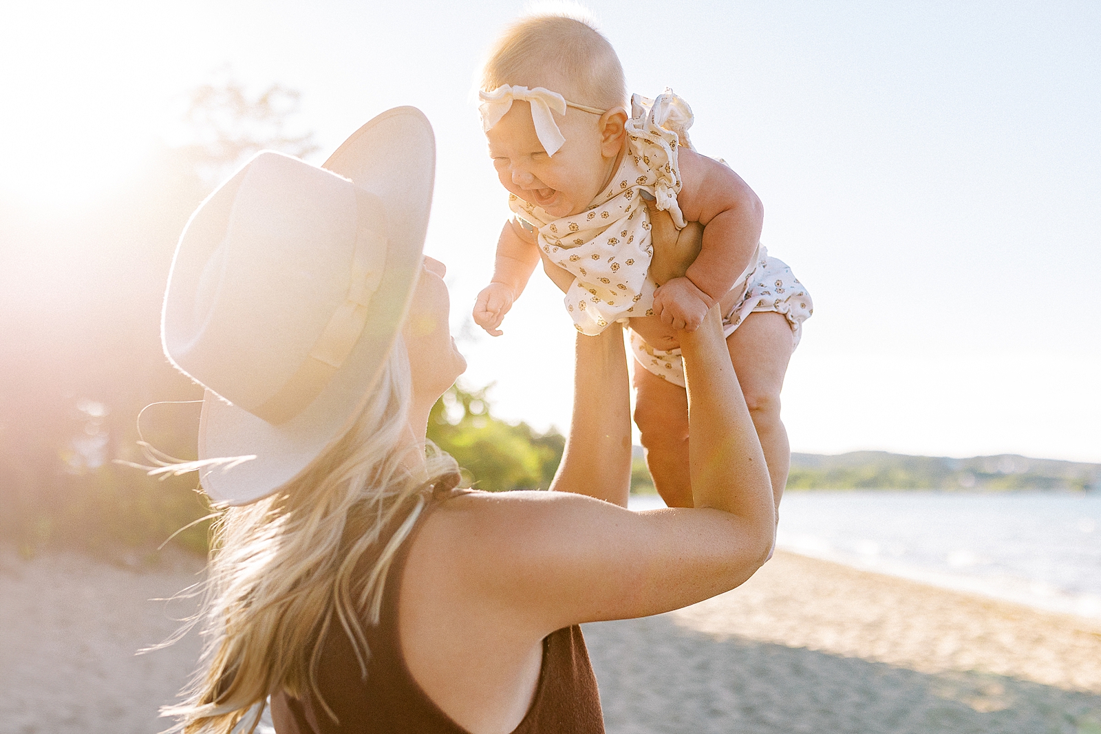 Image of Mom lifting Baby on the beach during a sunset family portrait session in Traverse City, Michigan.