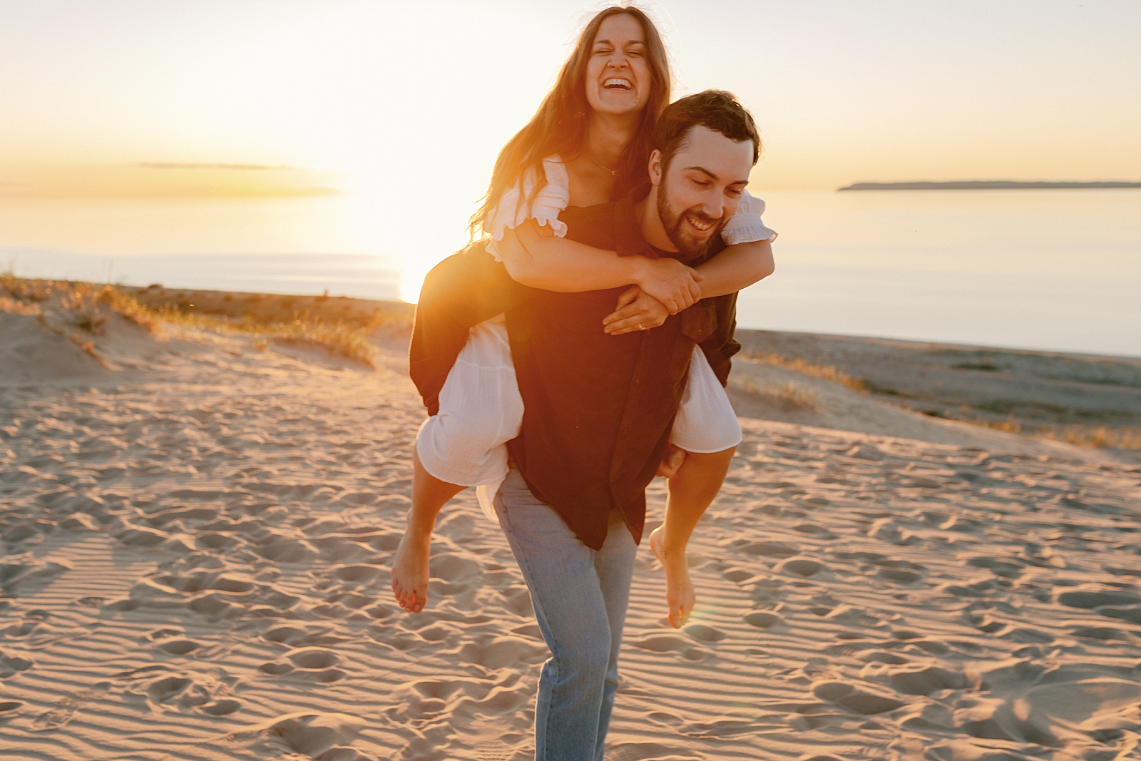 Playful piggyback ride during golden hour portraits in Sleeping Bear Dunes during Glen Arbor engagement session