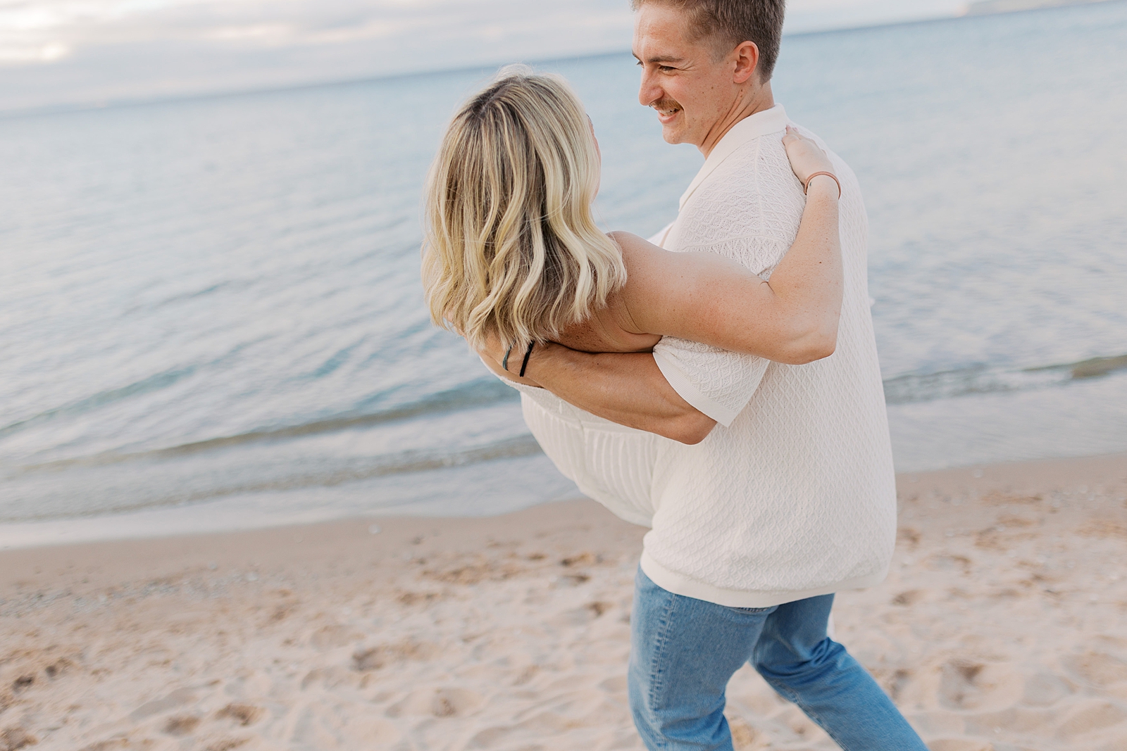 Man carrying woman during engagement session in Glen Arbor Michigan